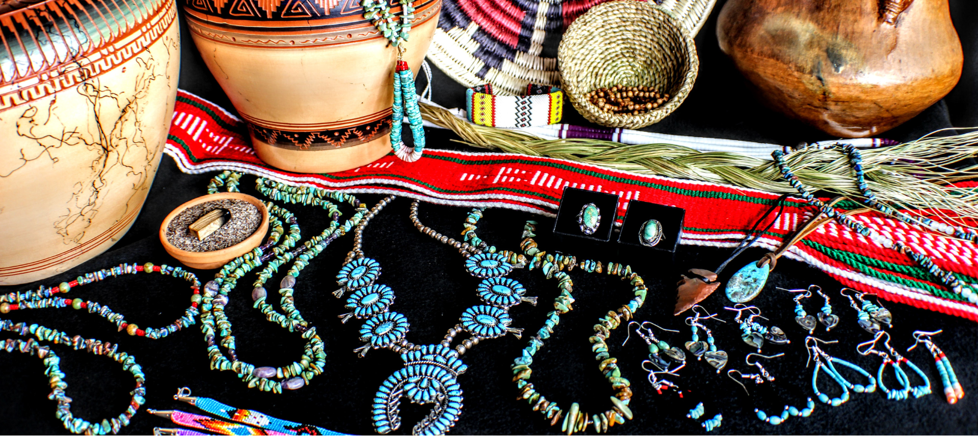Collection of Native American crafts including pottery, jewelry, and baskets on a dark surface.